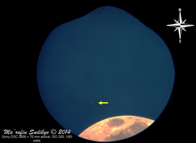 Gambar 1. Planet Saturnus (tanda panah kuning) sebagai segores garis cahaya redup di tengah langit yang masih terang benderang. Saturnus seakan mengambang di atas bagian Bulan yang hanya nampak sebagian saja di kawasan Mare Crisium dan sekitarnya. Diabadikan pada 4 Agustus 2014 dalam 10 menit sebelum terbenamnya Matahari dengan teknik afokal lewat eyepiece (okuler) 10 mm untuk kemudian diproses dengan GIMP 2. Sumber: Sudibyo, 2014. 