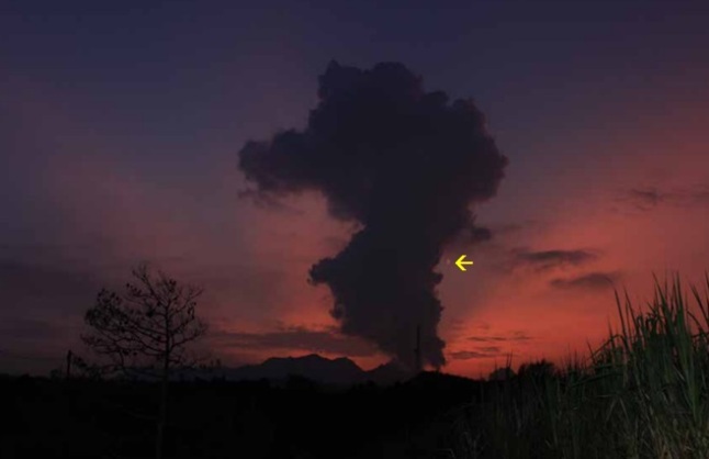 Gambar 1. Gunung Kelud pada Jumat 14 Februari 2014 TU jelang fajar dari kaki gunung sebelah barat. Nampak asap pekat masih mengepul dari kawah hingga setinggi beberapa ratus meter, beberapa jam pasca letusan besarnya usai. Pemandangan ini diterangi oleh semburat cahaya kemerah-merahan yang khas menjelang terbitnya Matahari. Planet Venus yang berada dalam kondisi paling terang (magnitudo -4,7) mengapung di atas horizon (tanda panah), menyaksikan kisah Bumi yang sedang bergulir. Sumber: Akhmad Zainuddin, 2014 dalam Geomagz, 2014. 