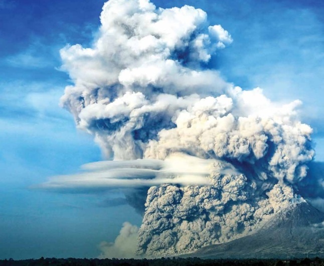 Gambar 1. Pemandangan menakjubkan, sekaligus mengerikan, saat Gunung Sinabung meluncurkan salah satu awan panas gugurannya ke arah lereng sektor tenggara dalam salah satu letusannya. Nampak jelas material awan panas yang berat dan bersuhu tinggi bergumpal-gumpal menuruni lereng. Tepat diatasnya debu vulkanik pekat mengepul ke atas membentuk awan debu vulkanik hingga ketinggian tertentu. Diabadikan oleh fotografer Hendi Syarifuddin pada 9 Februari 2015 TU dari arah kaki Sinabung sektor timur laut. Sumber: Syarifuddin, 2015 dalam Geomagz, Maret 2015. 
