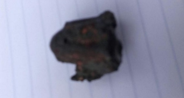 Gambar 3. Benda mirip meteorit seukuran 2 cm dengan berat 10 gram yang ditemukan di dasar lubang aneh. Nampak bagian sisi yang hangus. Sekilas terdapat bentuk mirip gelembung udara yang 'membeku' di permukaannya, morfologi yang mengingatkan pada regmaglif khas meteorit. Sumber: Kepolisian Tamil Nadu, 2016. 