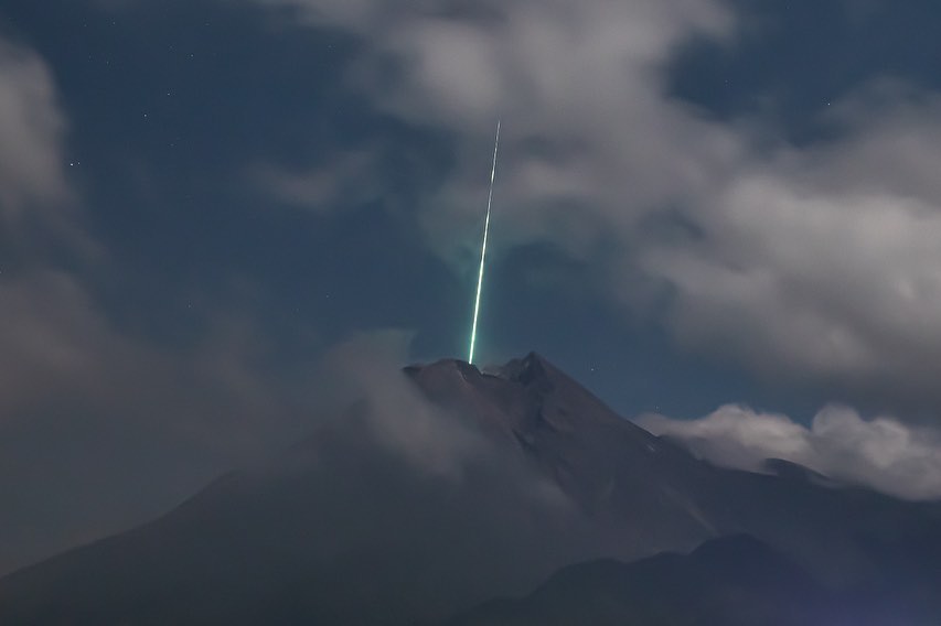 Gambar 1. Citra berkecepatan rana sangat lambat dari meteor-terang yang berimpit dengan puncak Gunung Merapi, diabadikan dari titik Kaliadem oleh Gunarto. Nampak meteor-terang diliputi oleh pendar warna kehijauan. Sumber : Gunarto, 2021. 
